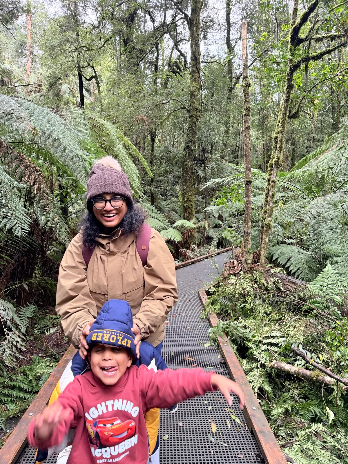 A mum and child exploring a fern-filled rainforest boardwalk